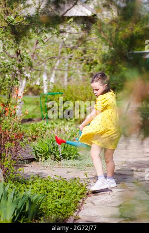 Ein sechsjähriges Kind in einem Kleid, das im Wind schwankt, blüht Blumen aus einem Garten, der von frühlingsblühenden Bäumen und Sträuchern auf einem umgeben ist Stockfoto