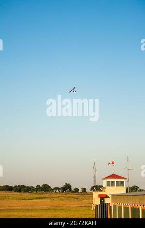 Motor-Hängegleiter mit Passagieren, die über den Flugplatz in klarem, blauem Himmel fliegen Stockfoto