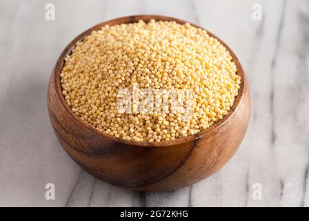 Eine Schale mit Vollhirse in einer Holzschale auf einer Theke aus weißem Marmor Stockfoto