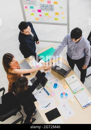 Eine Gruppe von vier Geschäftsleuten, die am Schreibtisch arbeiten und ihre Hände zusammenlegen, verspricht Teamarbeit und Einheitlichkeit. Stockfoto