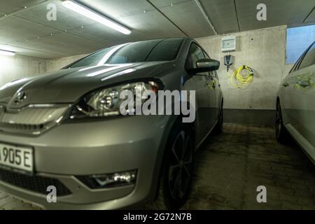 Elektroauto mit seinem typischen E am Nummernschild und einer Wallbox-Ladestation, die im Hintergrund an der Wand montiert ist. Stockfoto