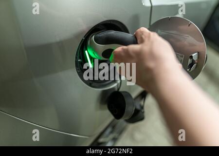 Detailansicht bei einer mans Hand mit ist das elektrische Ladekabel Plugin und Stecker in seine E-Autos Tankdeckel. Grünes Licht für das aktive Charhing Stockfoto