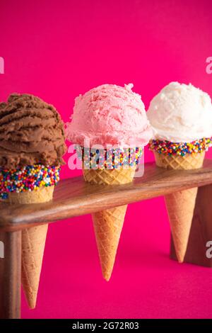 Schokolade Erdbeere und Vanille Eis Kegel mit Streuseln auf einem hellen rosa Hintergrund Stockfoto