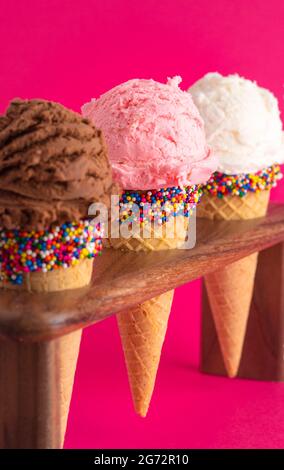Schokolade Erdbeere und Vanille Eis Kegel mit Streuseln auf einem hellen rosa Hintergrund Stockfoto