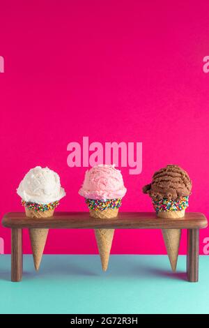 Schokolade Erdbeere und Vanille Eis Kegel mit Streuseln auf einem hellen rosa Hintergrund Stockfoto