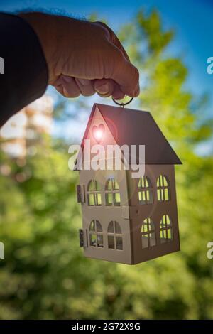 Housing Opportunity-Konzept mit einem Hausmodell, das an der Hand eines Mannes aus dem Nahen Osten hängt, mit einem Streulicht, das aus einem herzförmigen Loch kommt. Stockfoto