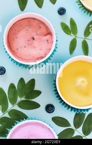 Sommerliche Lebensmittelkomposition mit verschiedenen hausgemachten, veganen, Fruchteis, Blättern und Blaubeeren auf blauem Hintergrund. Gefrorene Früchte Joghurt in Tassen - er Stockfoto