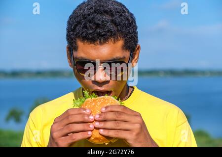 Afroamerikanischer Mann, der den Geschmack eines Hamburgers im Freien genießt Stockfoto