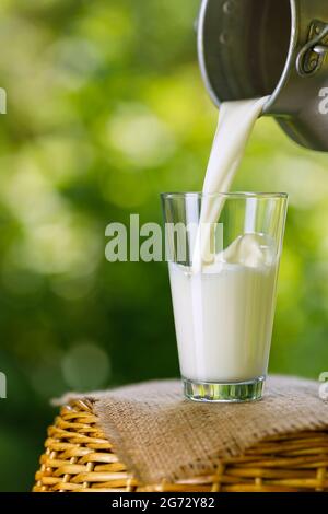 Milch, die aus Metallkännen in Glas gießt Stockfoto