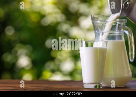 Milch wird aus Metallkannen in den Glaskrug im Freien gegossen Stockfoto