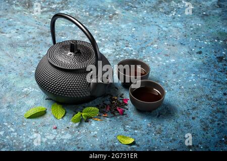 Schwarze japanische gusseiserne Teekane und Tee mit grünen Minzblättern auf blauem Betonhintergrund mit Kopierraum Stockfoto