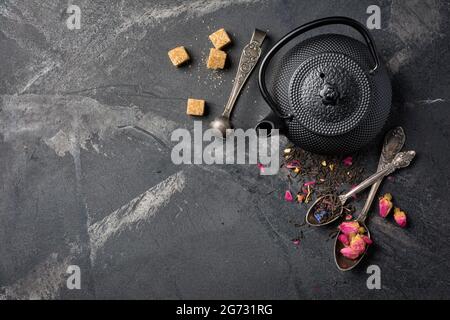 Draufsicht auf schwarzen asiatischen gusseisernen Wasserkocher und Tee mit Blütenblättern auf dunklem Marmorhintergrund mit Kopierfläche Stockfoto