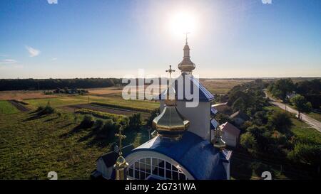 Luftaufnahme einer neuen modernen Kirche mit blauem Ziegeldach an einem Sommerabend in einem kleinen Dorf. Stockfoto