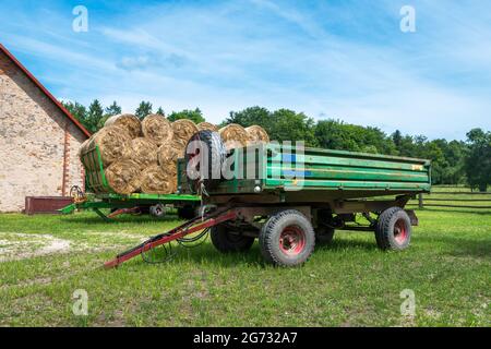 Alter, landwirtschaftlicher, grüner Anhänger, der in der Nähe des Heuballen- und Steingebäudes auf einem Bauernhof steht. Stockfoto