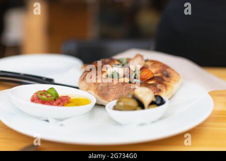 Italienische Focaccia mit Kirschtomaten, thassos-Oliven, Orangano, Olivenöl und Meersalz. Serviert mit Salsa und Oliven Stockfoto