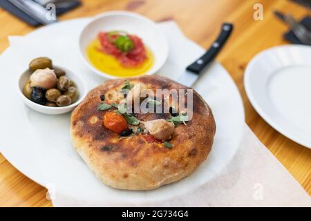 Italienische Focaccia mit Kirschtomaten, thassos-Oliven, Orangano, Olivenöl und Meersalz. Serviert mit Salsa und Oliven Stockfoto