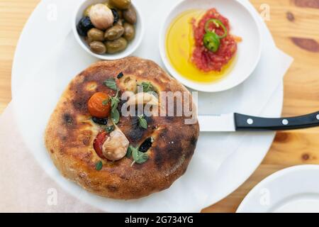 Italienische Focaccia mit Kirschtomaten, thassos-Oliven, Orangano, Olivenöl und Meersalz. Serviert mit Salsa und Oliven Stockfoto