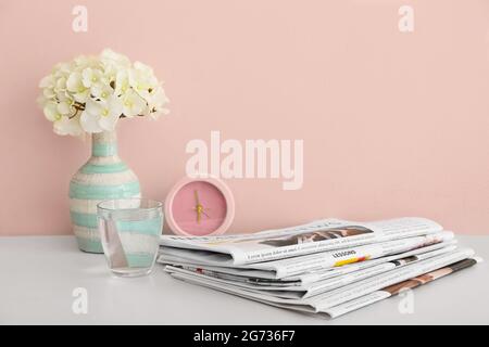 Zeitungen, Wecker und Vase mit Blumen auf dem Tisch neben der Farbwand Stockfoto