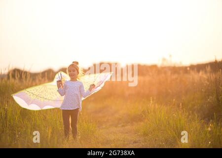 Mädchen steht mit Flügeln im Feld und lernt, einen Drachen zu fliegen. Outdoor-Unterhaltung im Sommer, Natur und frische Luft. Kindheit, Freiheit und Liebhaben Stockfoto