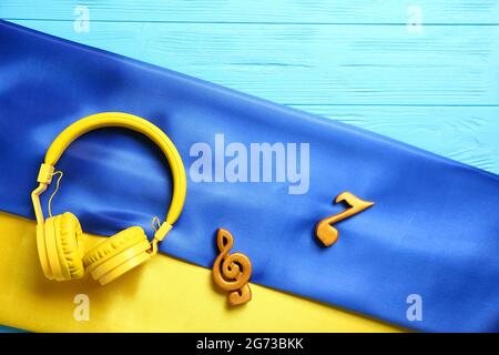 Musiknoten und Kopfhörer mit ukrainischer Flagge auf farbigem Holzhintergrund Stockfoto