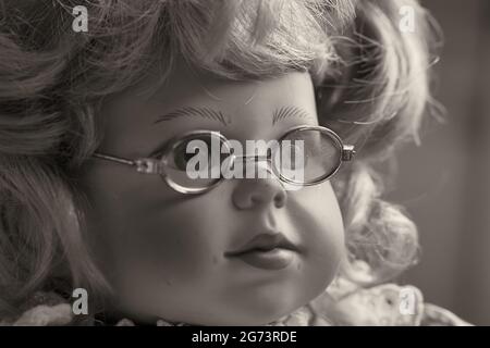 Porträt einer Vintage-Puppe, eines Spielzeugmädchen mit blondem Haar und Brille. Stockfoto