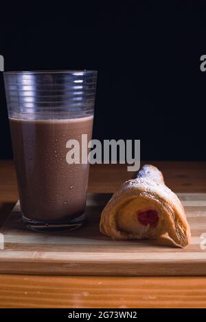 Eine leckere kegelförmige Süßigkeit und ein Glas Schokolade auf einem Holzbrett auf dem Tisch Stockfoto
