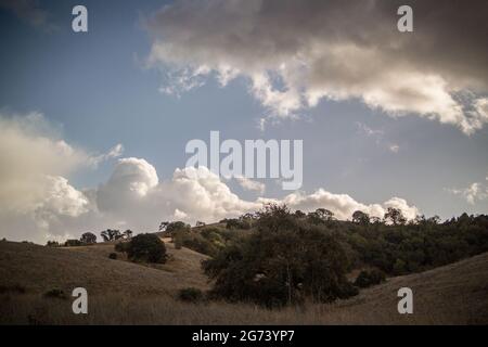 Strahlend blauer Himmel mit grauen Regenwolken, die Schatten über die Berglandschaft von Santa Cruz werfen. Stockfoto