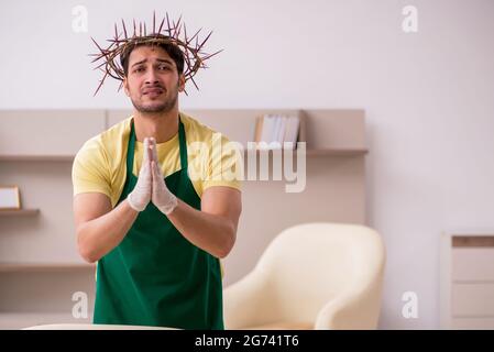 Junger männlicher Auftragnehmer, der auf dem Kopf einen stacheligen Kranz trägt und Hausarbeit leistet Stockfoto