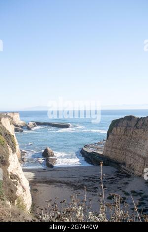 Kleine, schmale Bucht, umgeben von hohen, gestreifte Klippen, die Erosionswirkung zeigen. Sandküste, Offshore-Felsbank im Meer. Stockfoto