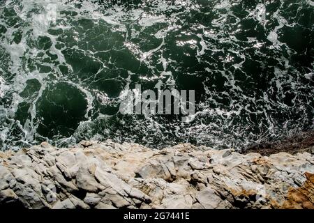 Blick über den Rand einer Klippe auf den grünen Ozean unten. Die Klippenkante bildet eine horizontale Linie über dem Foto. Land darunter. Meer oben. Stockfoto