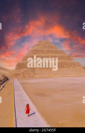 Eine junge Frau besucht die Stufenpyramide von Djoser Saqqara Ägypten unter bunten Wolken Stockfoto