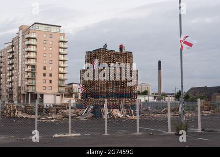 Belfast, Großbritannien. Juli 2021. Junge Männer sahen, wie der Bau des Lagerfeuers in der Sandy Row-Gegend abgeschlossen wurde. Am Lagerfeuer sind der Union Jack und die Ulster-Flagge angebracht. Um die Schlacht von Boyne zu feiern, werden in verschiedenen protestantischem Stadtteilen in Belfast Lagerfeuer errichtet. Die Lagerfeuer werden in der Nacht vor den Paraden des 12. Juli, am 11. Juli, angezündet. (Foto von Natalia Campos/SOPA Images/Sipa USA) Quelle: SIPA USA/Alamy Live News Stockfoto