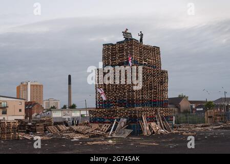 Belfast, Großbritannien. Juli 2021. Junge Männer sahen, wie der Bau des Lagerfeuers in der Sandy Row-Gegend abgeschlossen wurde. Am Lagerfeuer sind der Union Jack und die Ulster-Flagge angebracht. Um die Schlacht von Boyne zu feiern, werden in verschiedenen protestantischem Stadtteilen in Belfast Lagerfeuer errichtet. Die Lagerfeuer werden in der Nacht vor den Paraden des 12. Juli, am 11. Juli, angezündet. Kredit: SOPA Images Limited/Alamy Live Nachrichten Stockfoto