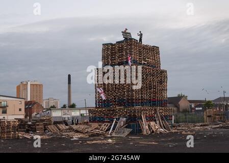 Belfast, Großbritannien. Juli 2021. Junge Männer sahen, wie der Bau des Lagerfeuers in der Sandy Row-Gegend abgeschlossen wurde. Am Lagerfeuer sind der Union Jack und die Ulster-Flagge angebracht. Um die Schlacht von Boyne zu feiern, werden in verschiedenen protestantischem Stadtteilen in Belfast Lagerfeuer errichtet. Die Lagerfeuer werden in der Nacht vor den Paraden des 12. Juli, am 11. Juli, angezündet. (Foto von Natalia Campos/SOPA Images/Sipa USA) Quelle: SIPA USA/Alamy Live News Stockfoto