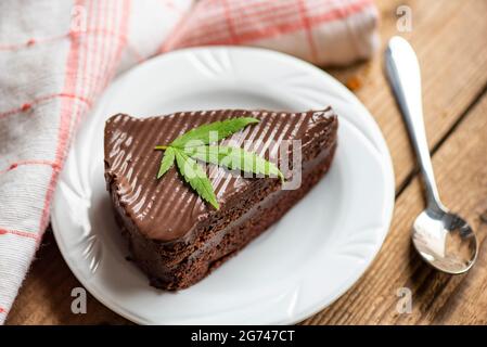 Schokoladenkuchen mit Cannabisblatt - Marihuanablätter Pflanze auf weißem Teller auf dem Holztisch, Cannabisfutter Natur Kräuter Konzept Stockfoto