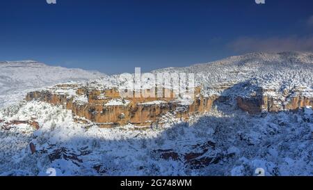 Schneebedeckte Siuranella-Klippen im Winter, vom Dorf Siurana aus gesehen. Im Hintergrund der Berg Montsant (Priorat, Tarragona, Katalonien, Spanien) Stockfoto