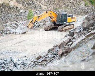 Orange Bagger arbeitet an Erdarbeiten im Tagebau. Yellow Backhoe gräbt Sand und Kies im Steinbruch. Maschinen für schwere Baumaschinen in AC Stockfoto