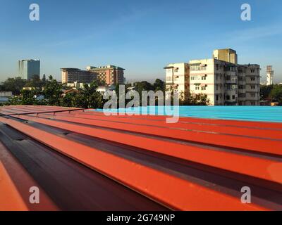 Rot und blau lackiertes Dachblech vor einem Blick auf Bangalore Stadt im Hintergrund Stockfoto