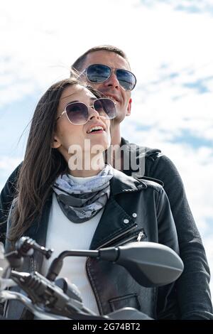 Schöner Kerl und schönes Mädchen in Sonnenbrille. Ein paar junge lächelnde fröhliche Biker. Zwei kaukasische Menschen sitzen auf dem Motorrad. Vertikal sh Stockfoto