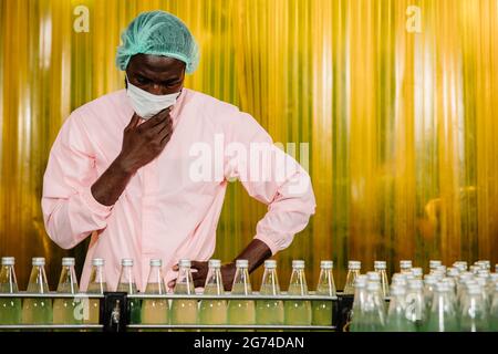 Afrikanischer Schwarzmann Arbeiter Arbeit in der Lebensmittel-und Getränkeindustrie Fabrik mit Hygienearbeit Fruchtsaft Produktionslinie Inspektor Mitarbeiter. Stockfoto