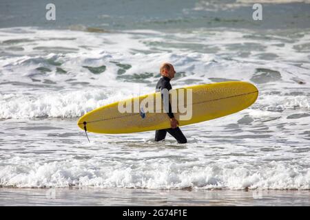 Australischer Surfer mittleren Alters in Neoprenanzug trägt sein Surfbrett im Ozean, Sydney, NSW, Australien Stockfoto