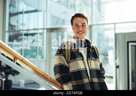 Student an der College-Treppe lächelnd. Ein junger Mann lächelt der Kamera zu, während er sich an einem Treppengeländer in der Universität lehnt. Stockfoto