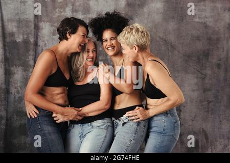 Schöne Frauen unterschiedlichen Alters lachen zusammen in einem Studio. Vier verschiedene und körperpositive Frauen feiern ihren natürlichen Körper, während sie J tragen Stockfoto