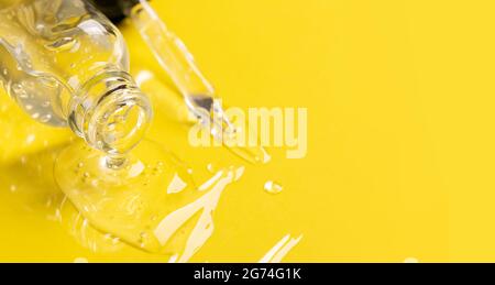 Kosmetisches flüssiges Gel-Serum-Gleitmittel fließt aus der Glasflasche Tropferflasche auf gelbem Hintergrund. Gesichts- und Körperpflege Stockfoto