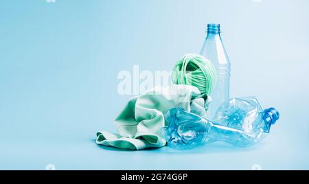 Leere Plastikflasche und verschiedene Stoffe aus recyceltem Polyesterfaser-Synthetikgewebe auf blauem Hintergrund Stockfoto