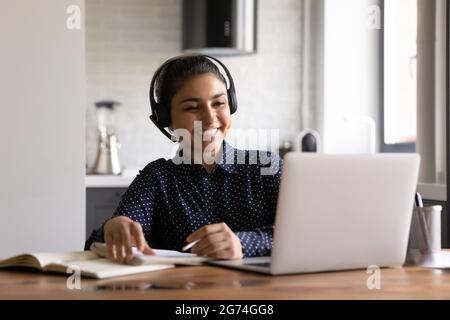 Glücklicher indischer Student in Kopfhörern mit Mikrofon, der an einem virtuellen Training teilnimmt Stockfoto