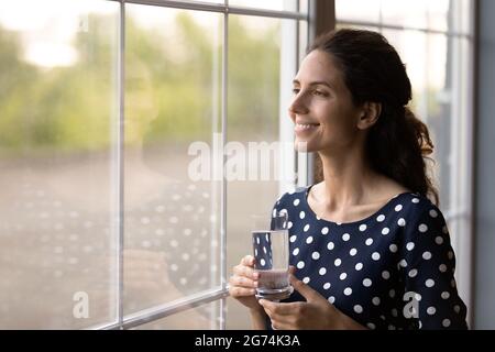 Glückliche lateinische Frau in zwangloser Holding Glas von reinem frischem Trinkwasser Stockfoto