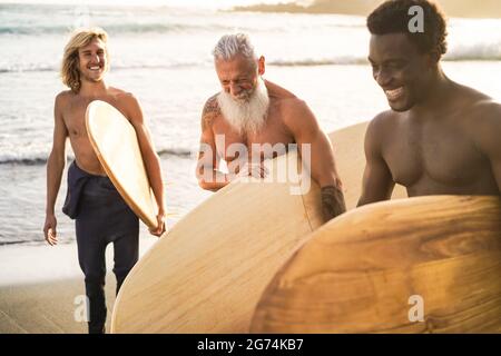 Surfer-Freunde mit mehreren Generationen, die nach der Surfstunde am Strand Spaß haben – konzentrieren Sie sich auf das Gesicht eines älteren Mannes Stockfoto