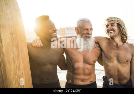 Surfer-Freunde mit mehreren Generationen, die nach der Surfstunde am Strand Spaß haben – konzentrieren Sie sich auf das Gesicht eines älteren Mannes Stockfoto