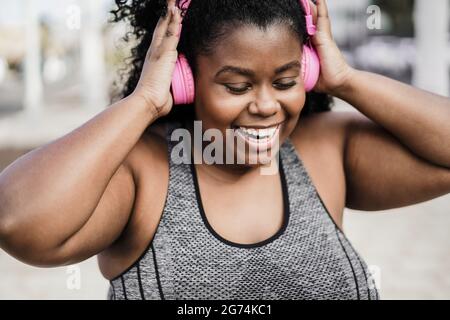 Happy Sport kurvige schwarze Frau hört Musik mit Kopfhörern - Fokus auf Gesicht Stockfoto